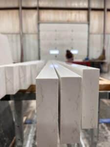 IMG-20260506-WA0054 - Stone Fabricator Solutions Close-up of white marble-textured rectangular blocks standing upright in a workshop or warehouse setting, with a blurred background.