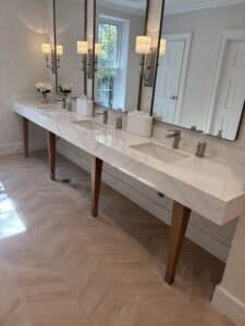 TVOR Vanity Top 2 - Stone Fabricator Solutions Double vanity with marble countertop, two sinks, and tall mirrors in a bright, modern bathroom.