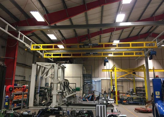Industrial workshop with a large yellow overhead gantry crane system, metal framework, and various machinery on the floor.