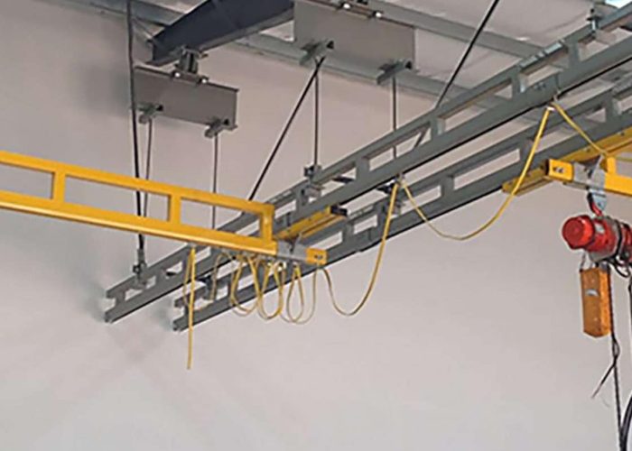 Overhead hoist system with a red motorized trolley and yellow cables hanging from metal track in a workshop
