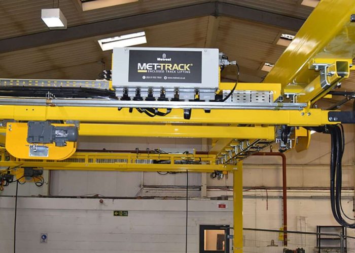 Yellow overhead crane rails with a MET-TRACK control unit in a factory setting