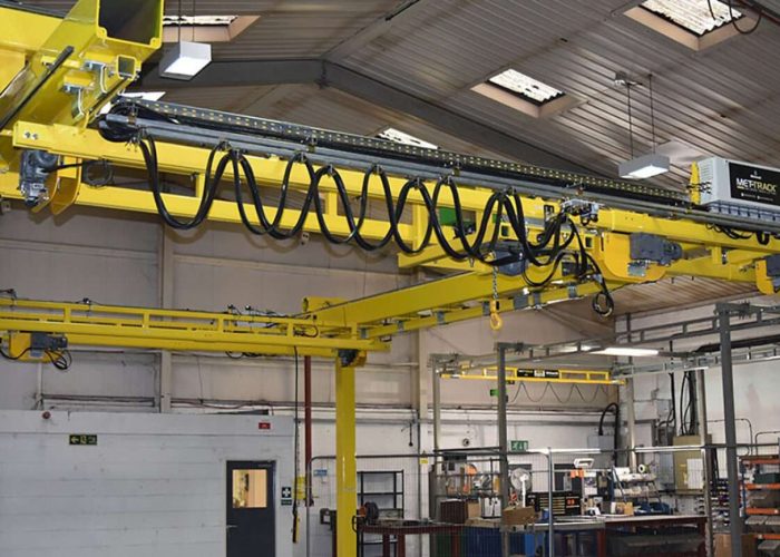 Yellow overhead crane system and track in a bright factory workshop with cables hanging from the beam.